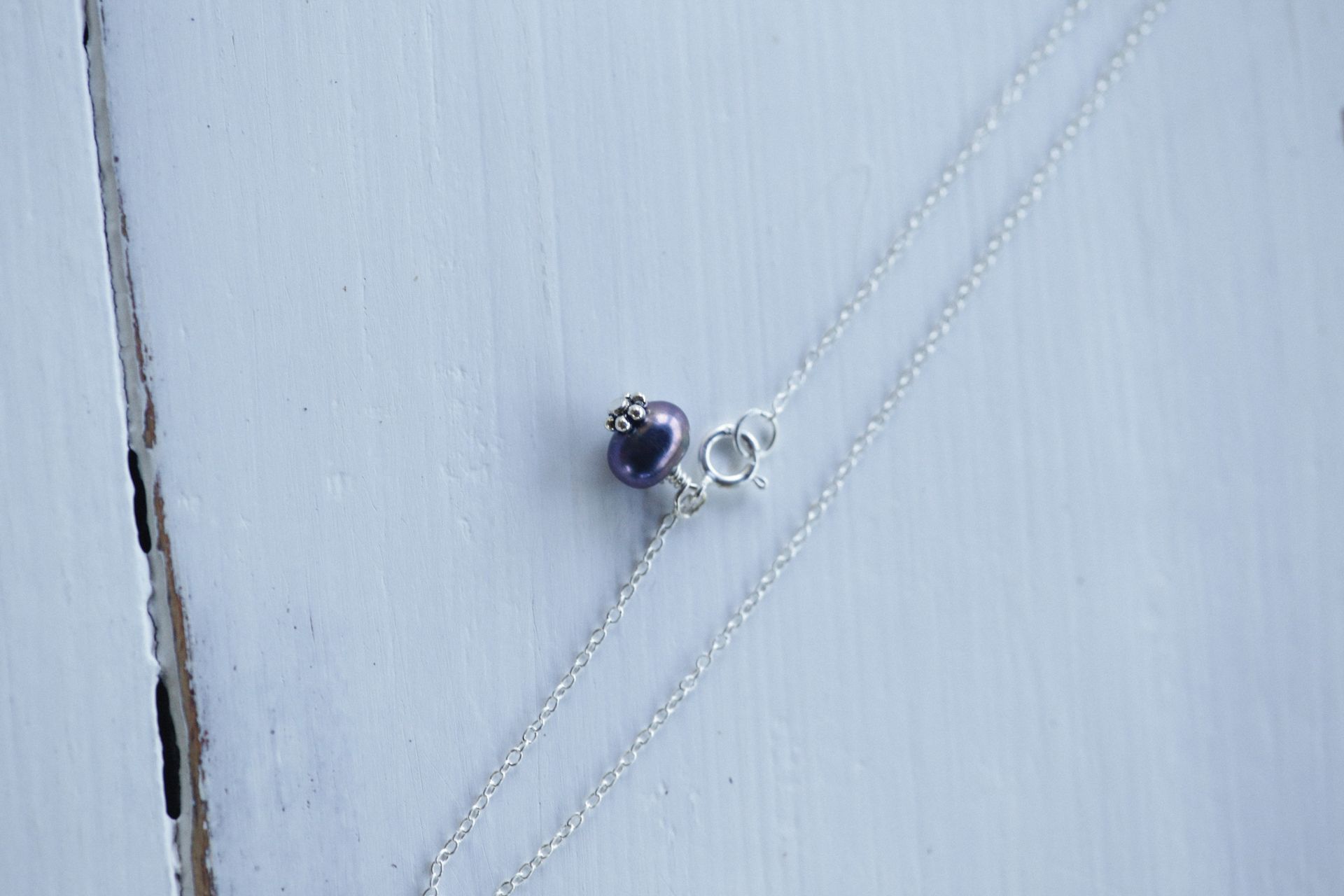 Close-up of a silver necklace with a purple bead pendant on a wooden surface.