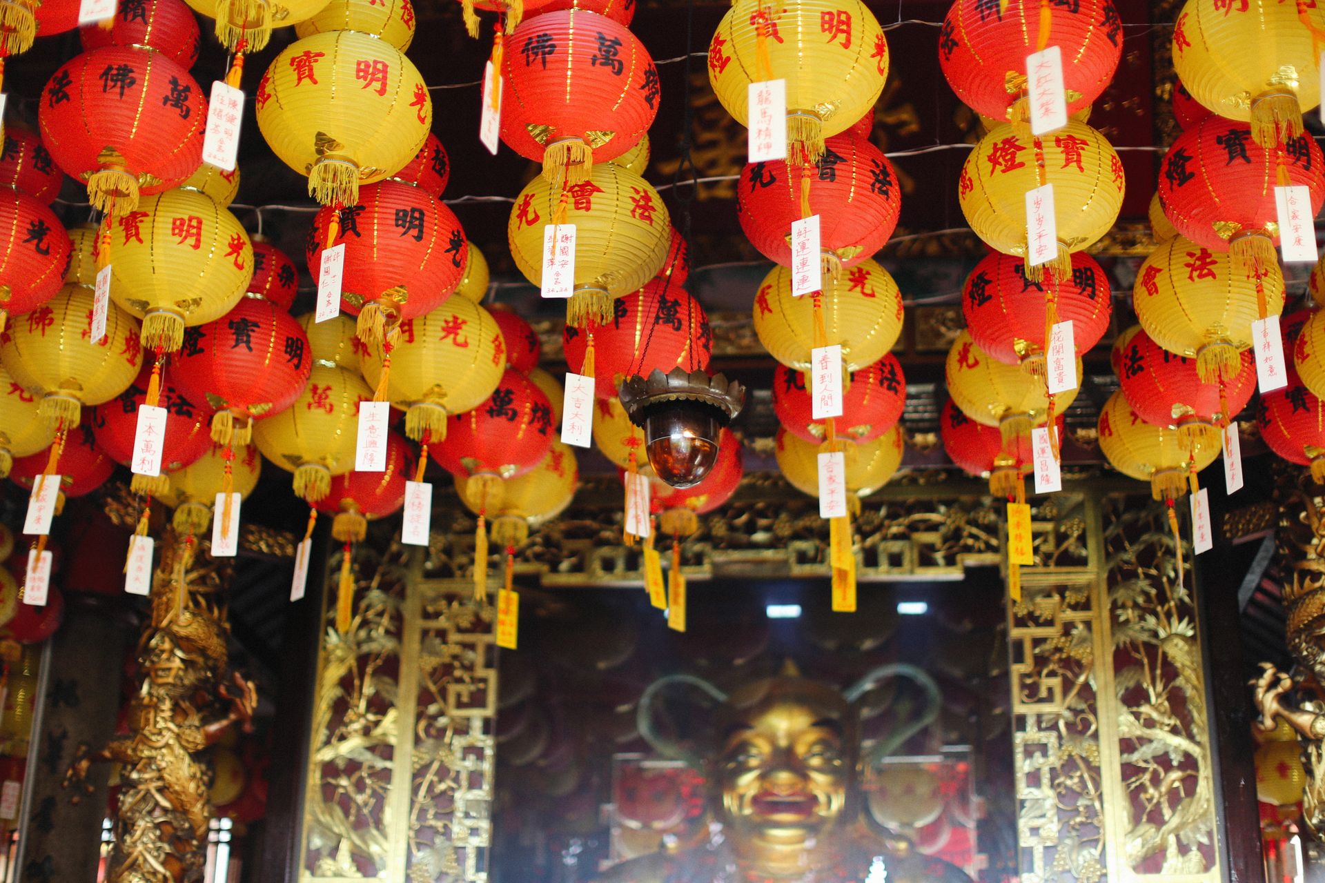 Colorful red and yellow Chinese lanterns hanging in a richly decorated temple.