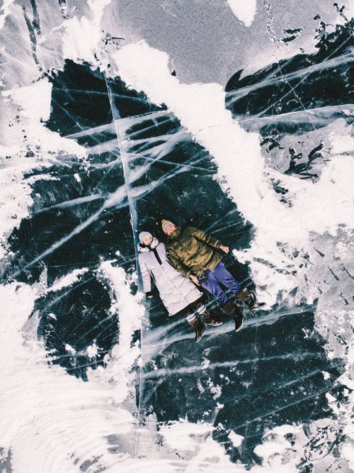 Free Couple in winter clothing lying on a frozen lake with visible ice patterns. Stock Photo