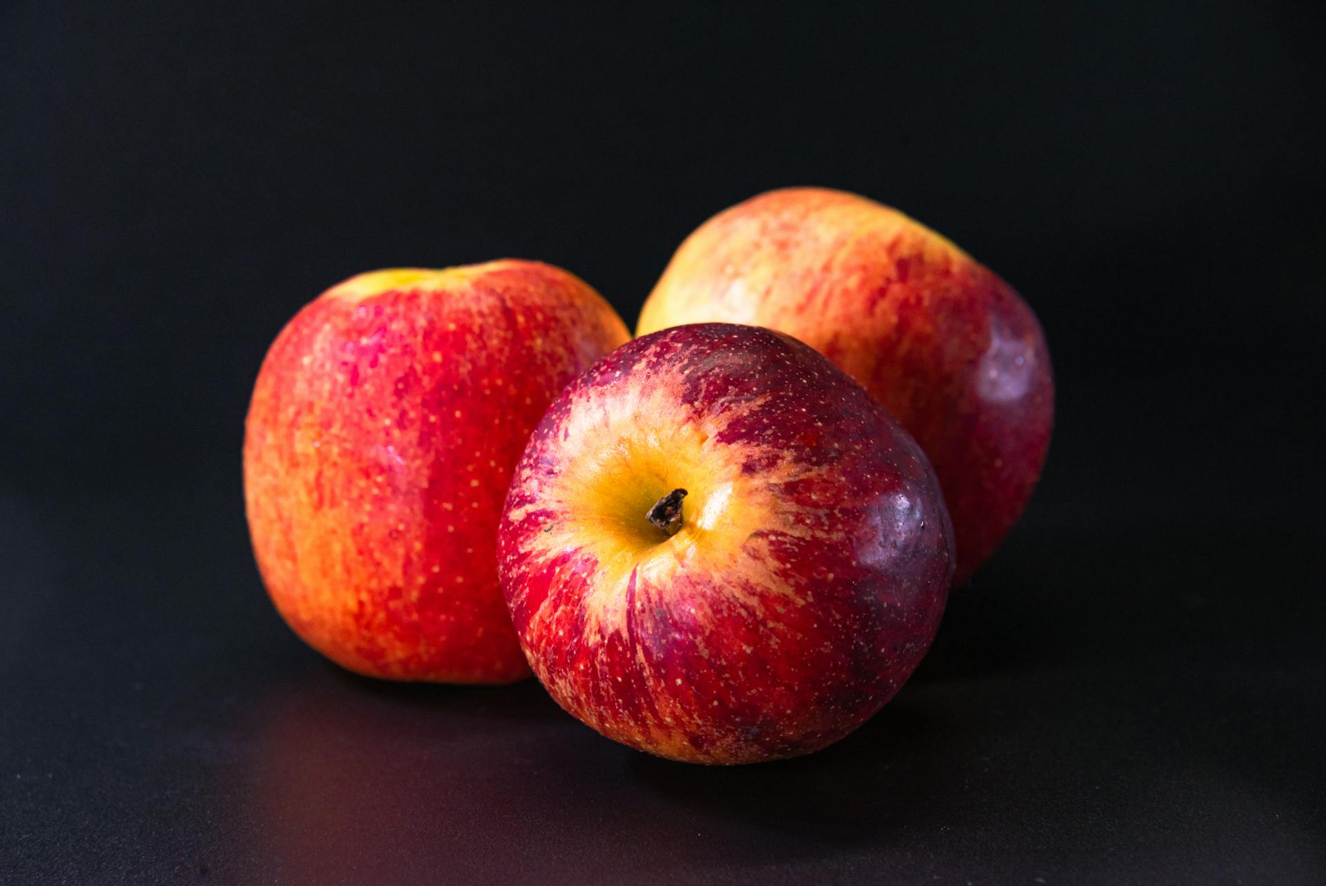 Three vibrant red apples on a dark surface, perfect for fruit and healthy living themes.