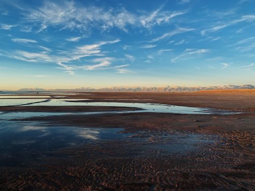 Free A breathtaking sunset over a tranquil beach with reflections on the water and distant mountains. Stock Photo
