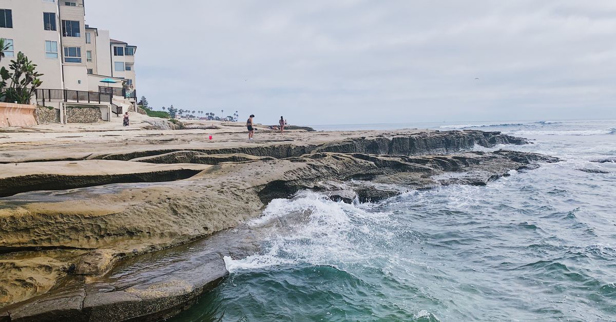 A scenic view of waves crashing on a rocky shoreline near a coastal resort.