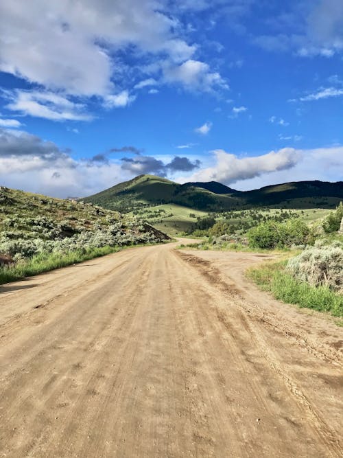 Brown Dirt Road Between Green Grass Field Under Blue Sky