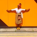 一位身着阳光时尚、充满活力的女人在户外亮黄色的墙壁前摆姿势