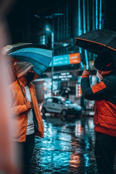 Two men with umbrellas on a rainy night in Kathmandu, Nepal, under neon street lights.