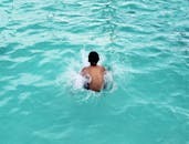 一个小男孩在充满活力的蓝色泳池中畅游，溅起清爽的水花