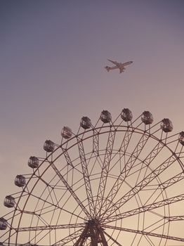 A commercial airplane flies over a Ferris wheel during twilight, creating a serene and captivating scene.