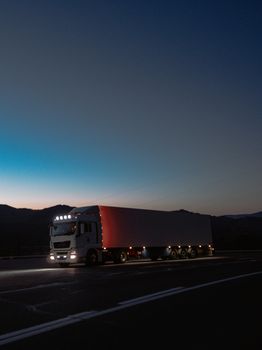 A large truck travels on a highway at dusk surrounded by mountains, showcasing travel and logistics.