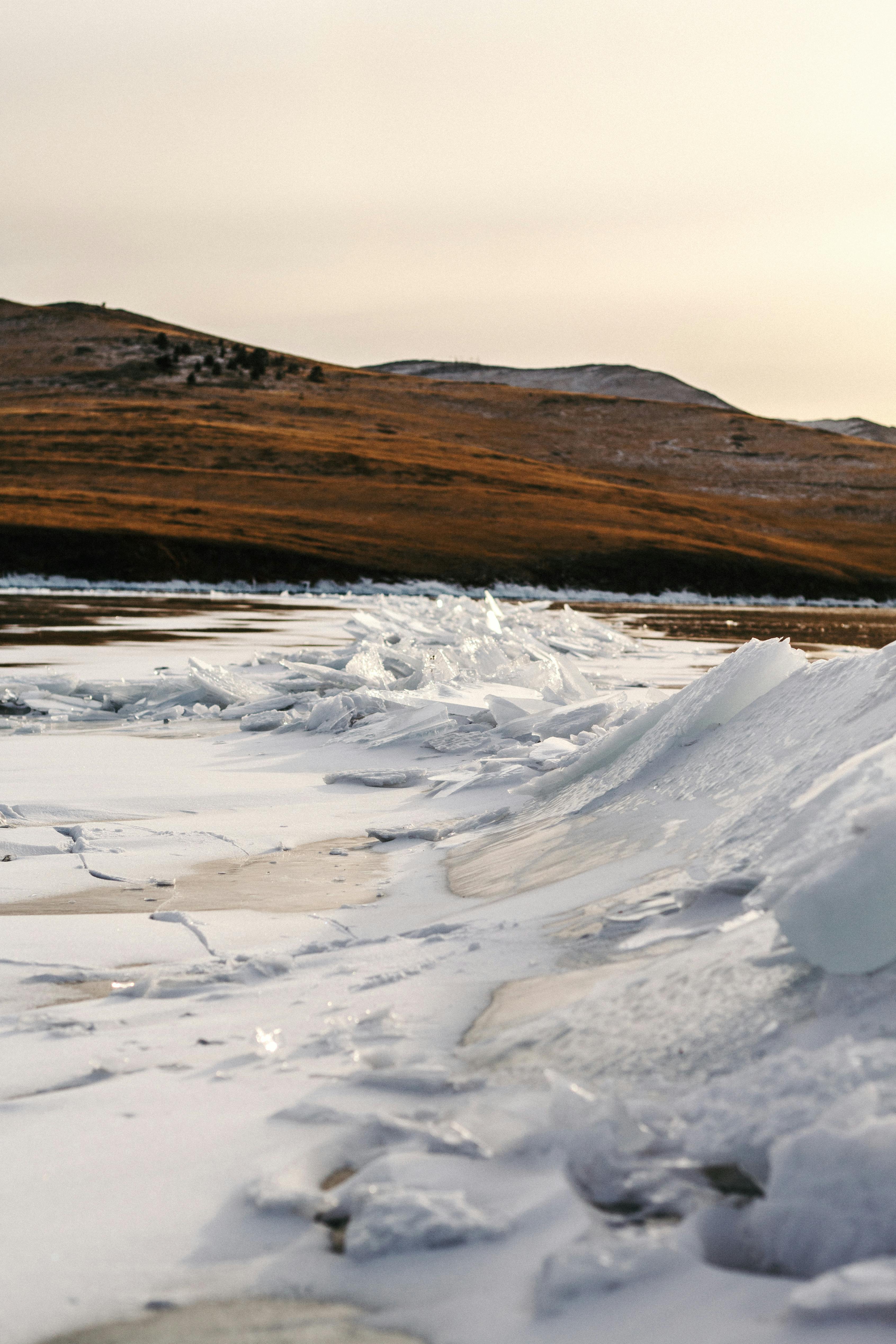 Winter landscape featuring a frozen river with ice formations against distant hills.