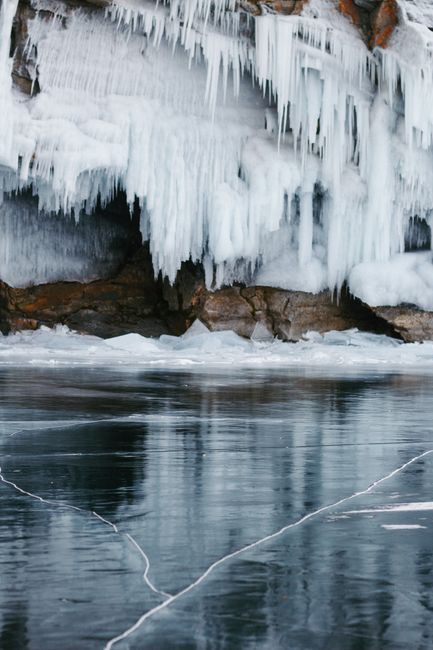A serene winter landscape featuring a frozen lake and dramatic icicles over rocky terrain.