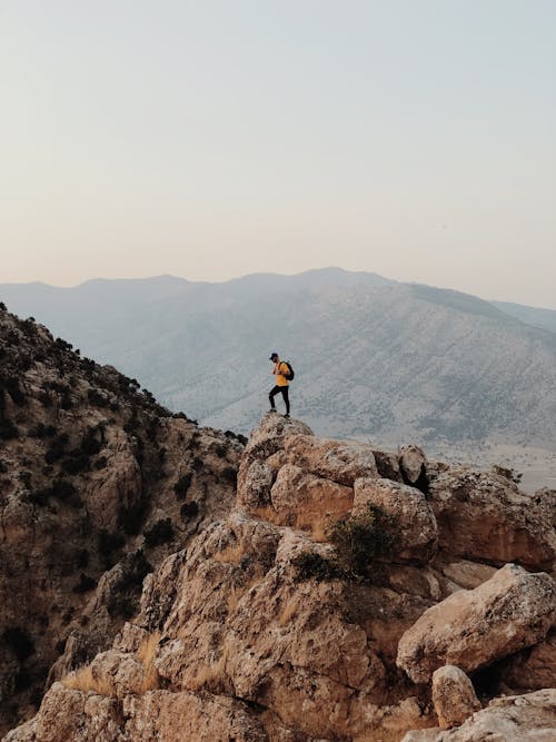 Person Standing on Top of a Brown Rock Mountain