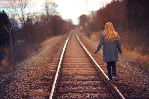Woman in Blue Jacket and Blue Jeans Walking on Train Track Photography
