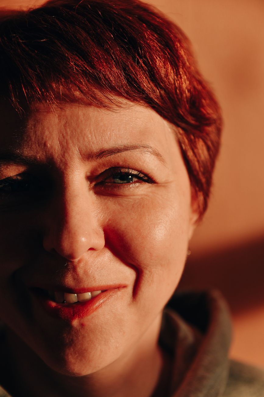 Close-up portrait of a smiling woman with red hair in warm light.