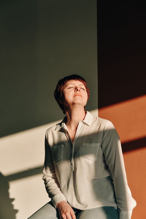 Free A woman enjoying sunlight indoors, eyes closed and feeling at peace. Stock Photo