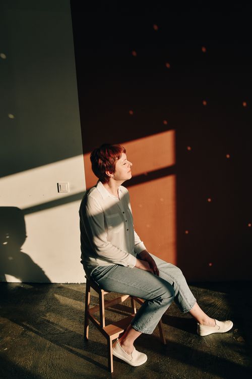 Free A woman sitting peacefully indoors, enjoying sunlight and shadow play on the wall. Stock Photo