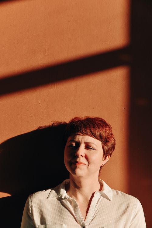 Free Woman standing against a warm-toned wall with shadows, expressing thoughtful emotion. Stock Photo
