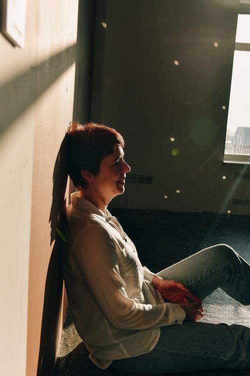 Free A woman with short hair relaxes against a wall in soft sunlight inside a room. Stock Photo