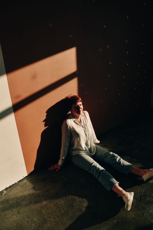 Free A woman with short hair sits on the floor, enjoying sunlight and shadows indoors. Stock Photo