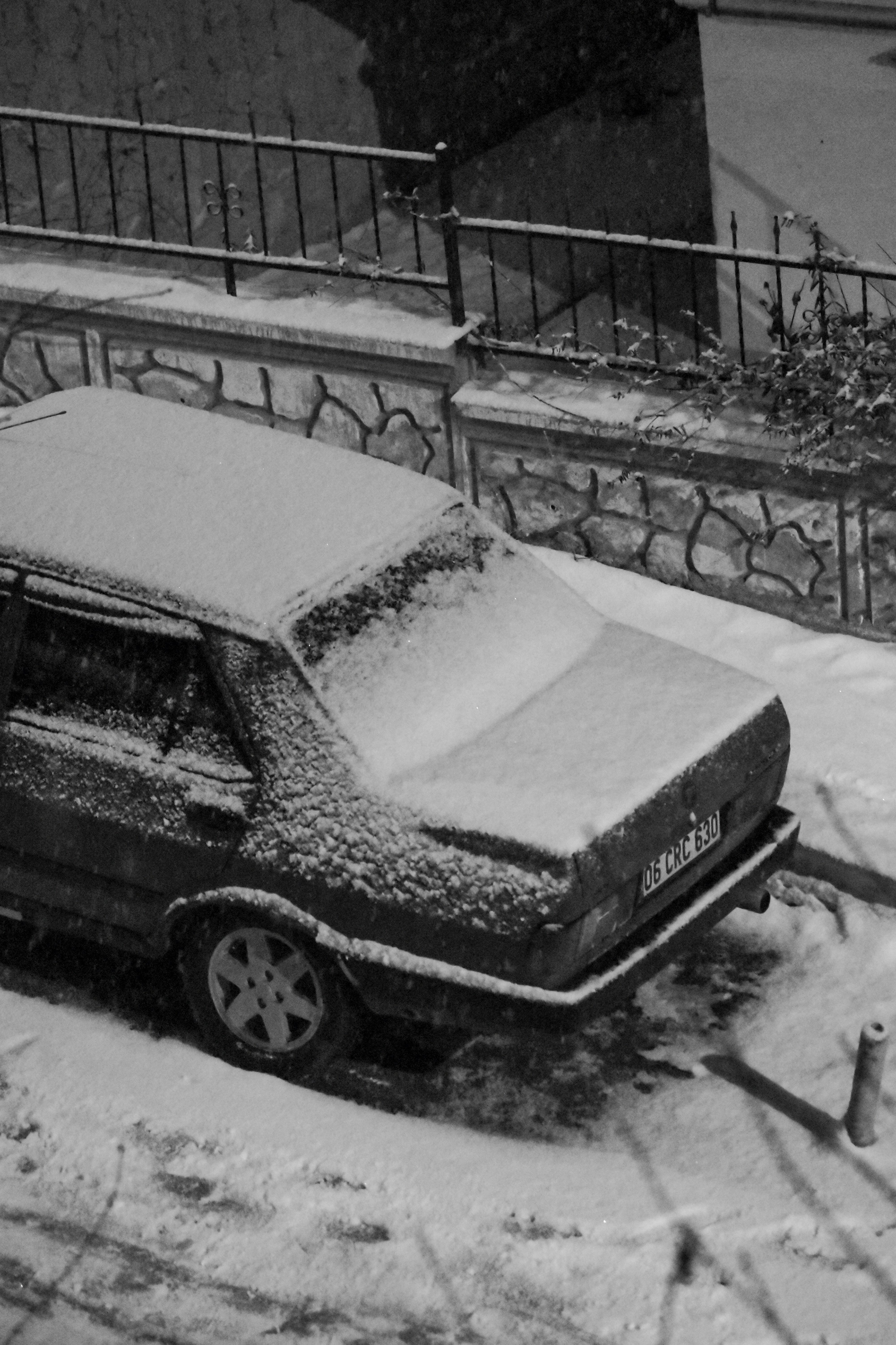 Vintage car covered in snow during a serene winter night, captured in monochrome.