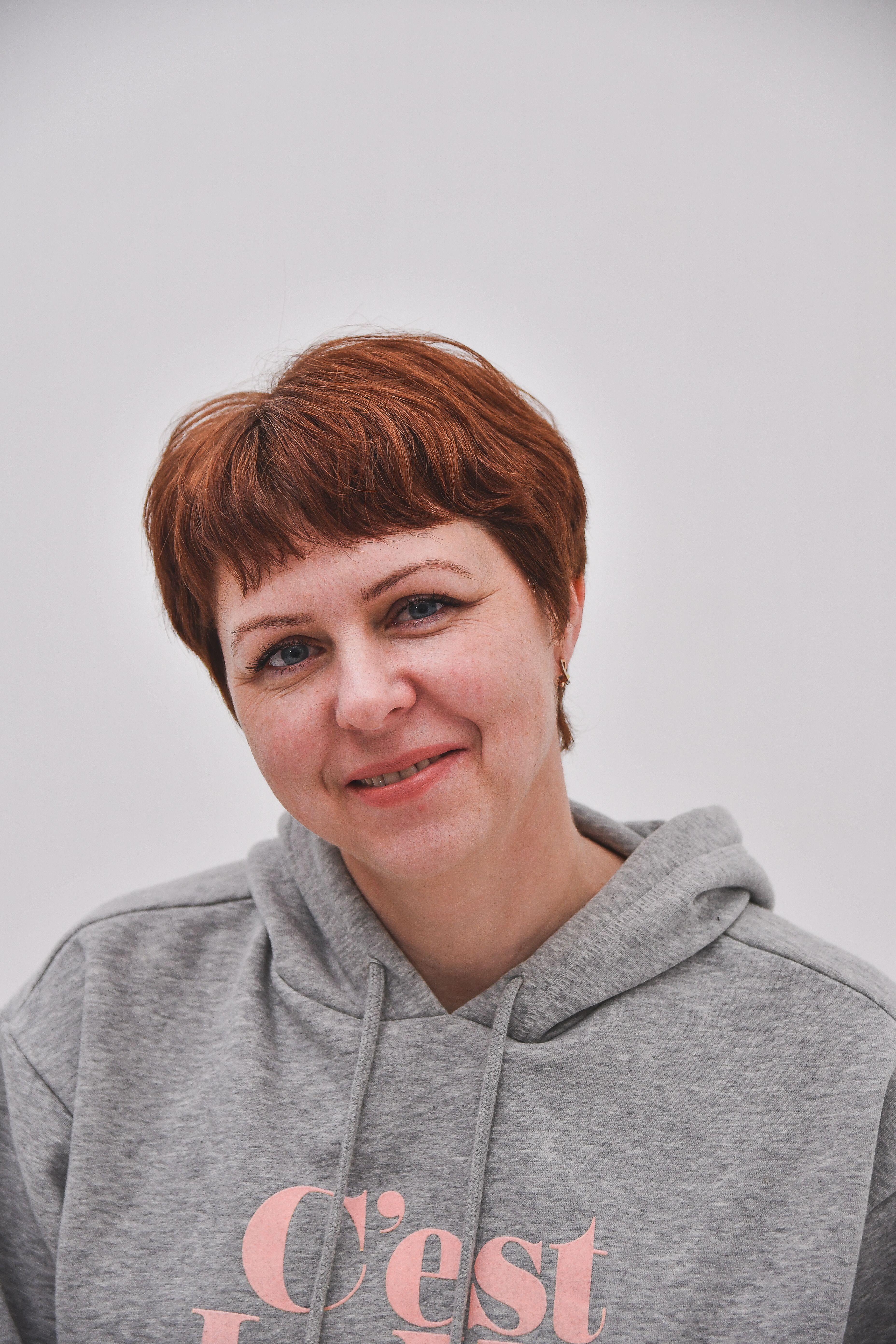 Cheerful woman with short hair smiling in a grey hoodie against a white background.