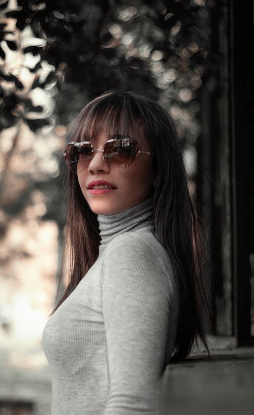 Free Portrait of a woman outdoors wearing sunglasses and a gray turtleneck, smiling confidently. Stock Photo