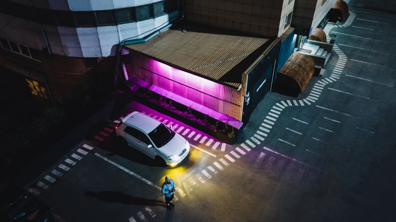 Aerial shot of a parking lot at night in Novosibirsk with vibrant purple lighting accentuating a parked white car.