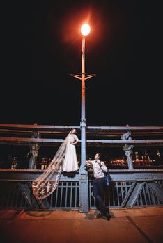 Elegant couple captured in a romantic nighttime wedding photoshoot on a historic Wrocław bridge.