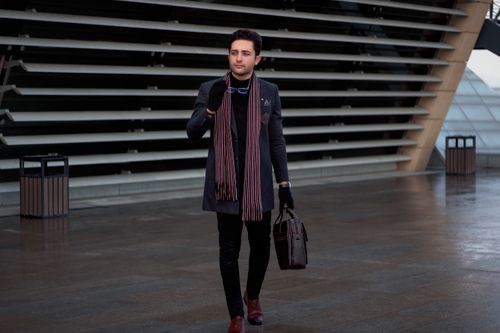 Free A fashionable man with a briefcase and scarf walking near modern architecture in Tehran. Stock Photo
