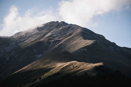 Free A stunning mountain peak casting shadows under a clear sky with clouds. Stock Photo