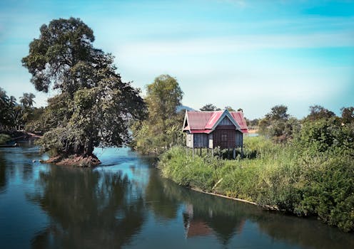A serene scene of a stilt house on a lush riverbank, reflecting tranquility and nature's beauty.