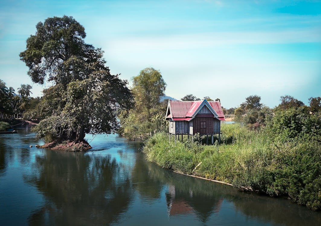 Free A serene scene of a stilt house on a lush riverbank, reflecting tranquility and nature's beauty. Stock Photo