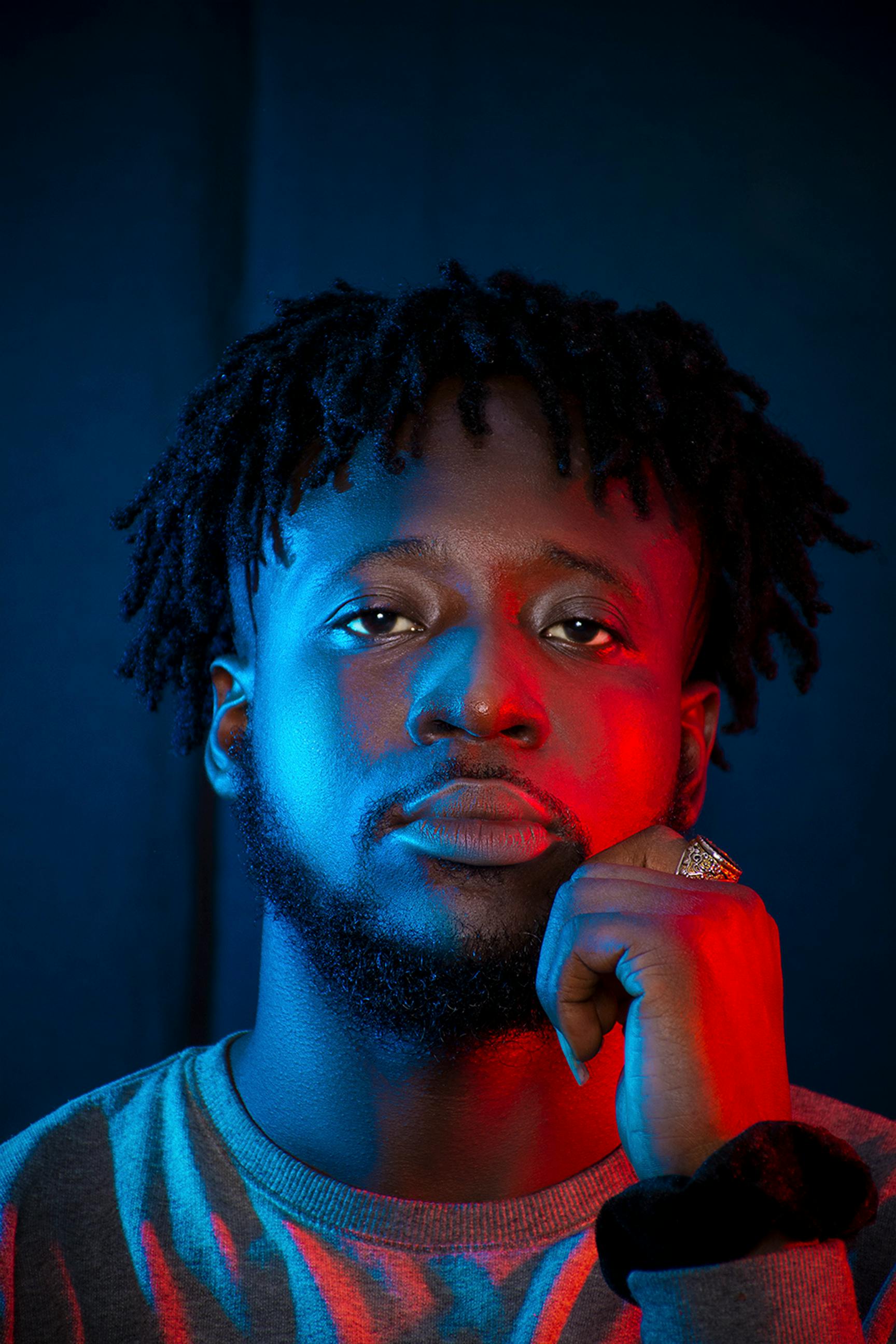 Striking portrait of a confident man with dreadlocks, highlighted by bold red and blue lighting.