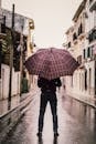 Person Wearing Black Pants Holding Umbrella Standing On Road