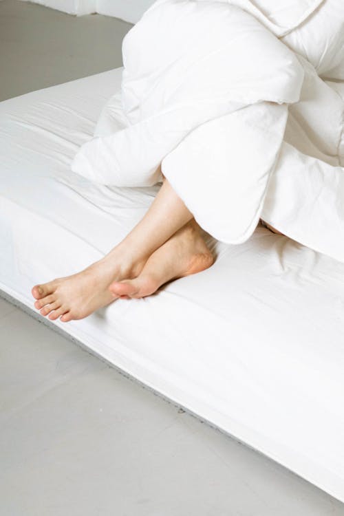 Free Person Wrapped in Duvet Resting Feet on Mattress Stock Photo