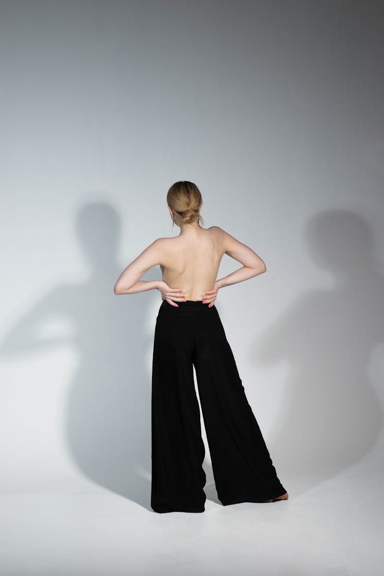 Shirtless Woman In Wide Pants Casting Shadows On Wall