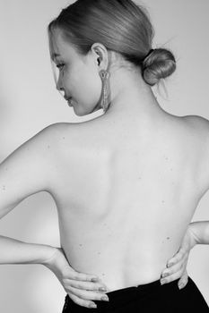 Black and white portrait of an elegant woman with hair bun and earrings, seen from behind.