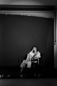 Graceful woman sitting in a stylish chair in a black and white studio setting, exuding elegance and poise.