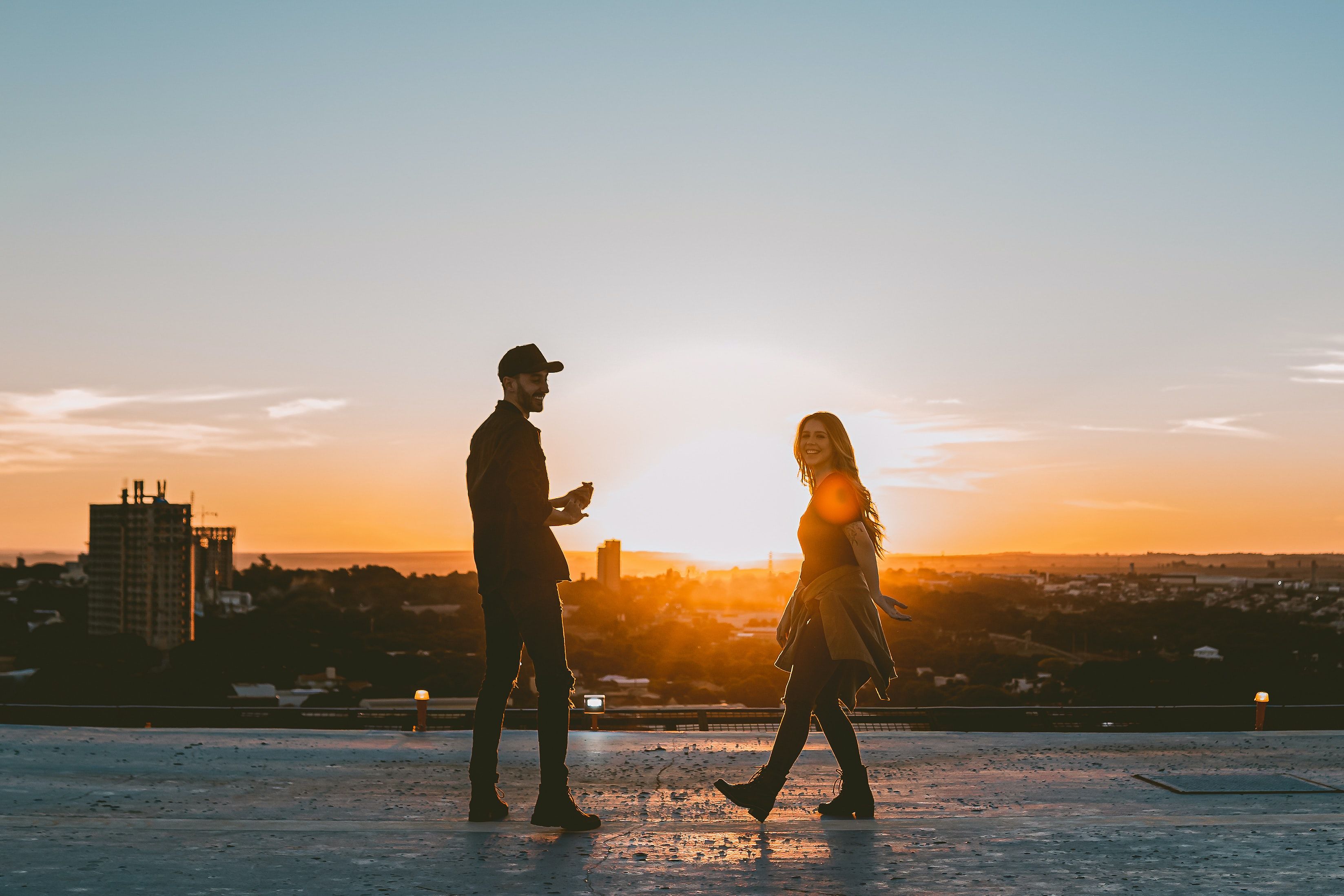 Smiling couple stands on rooftop, enjoying a warm sunset together.