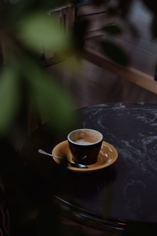Free A warm cup of cappuccino on a marble table amidst lush greenery for a cozy cafe vibe. Stock Photo