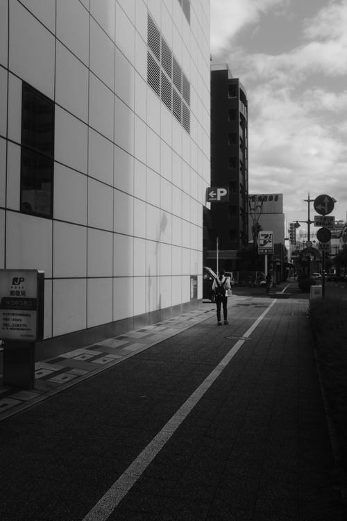 Free A monochrome view of a city street with a single person walking along the sidewalk. Stock Photo