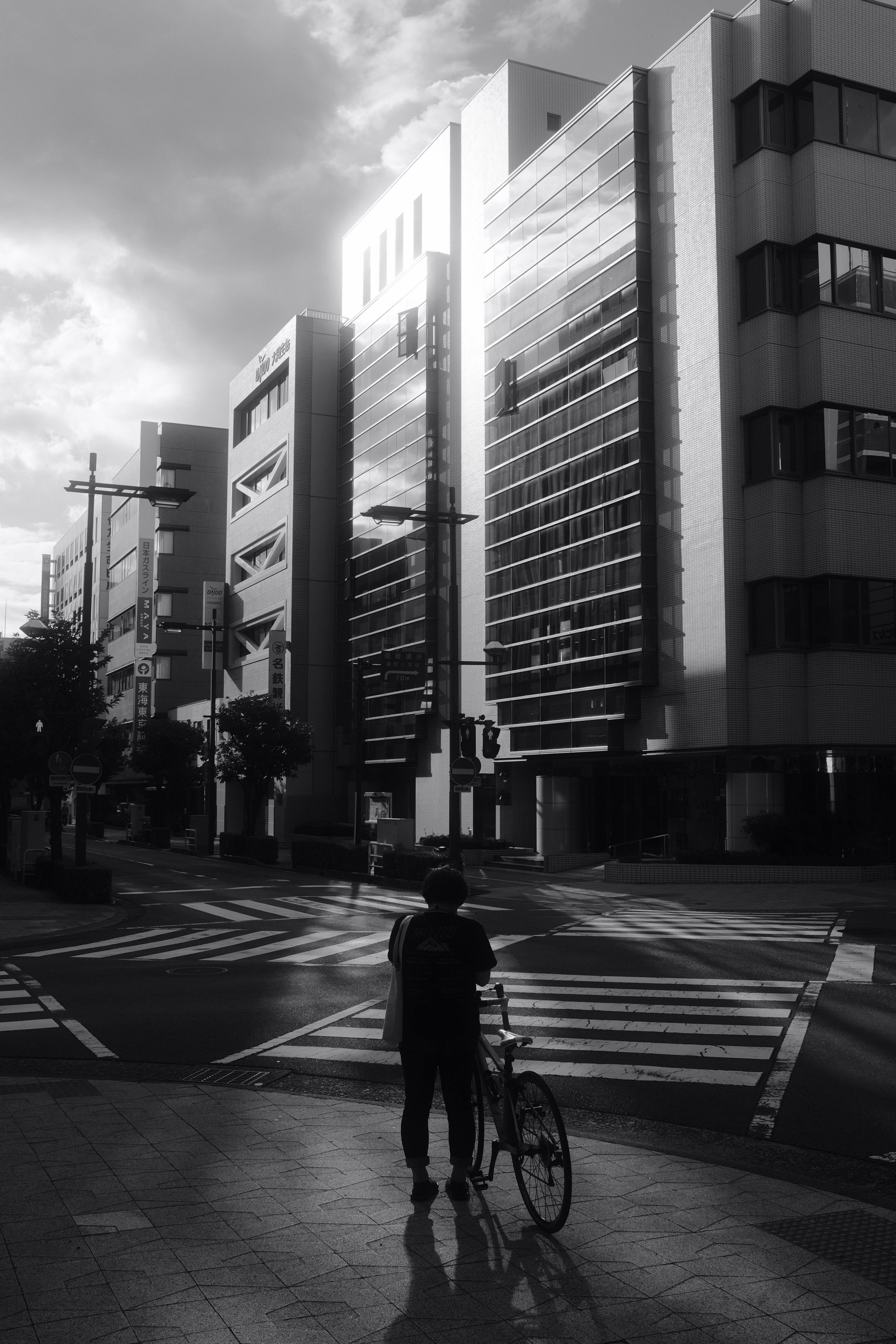 Black and white photo of a cyclist waiting on a city crosswalk.