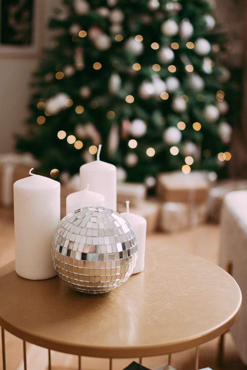 Free Elegant Christmas setting with candles and disco ball on table by tree. Stock Photo