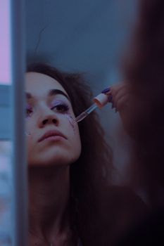 A woman carefully applies makeup with a dropper in front of a mirror, capturing her reflection.