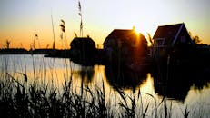 日落时分，湖畔景色宁静，房屋的轮廓和芦苇倒映在水面上