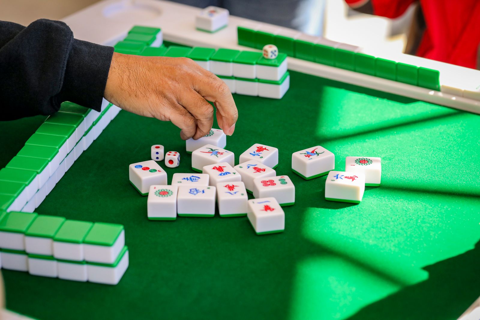 Close-up of hands playing mahjong on a green table