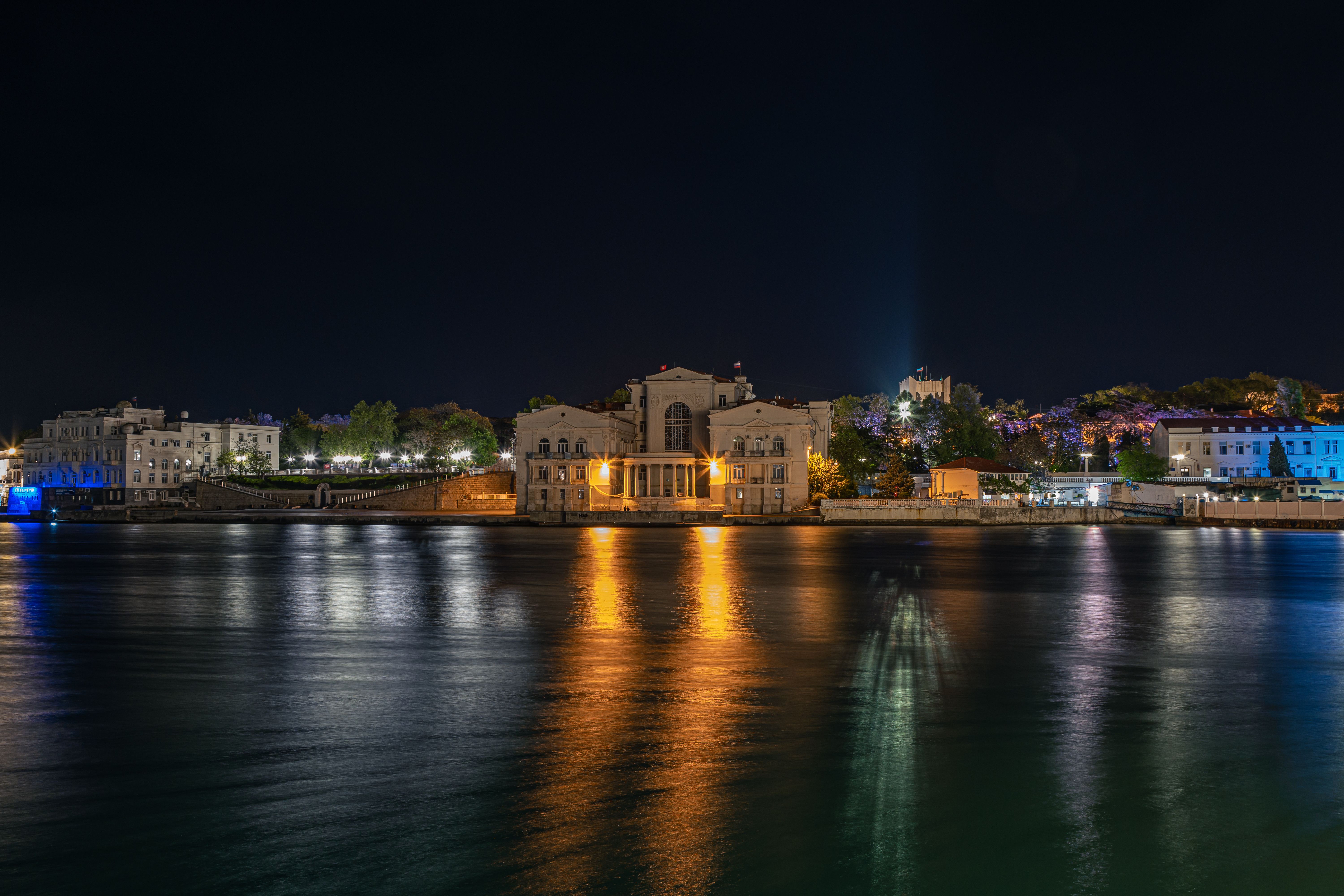 Night view of illuminated buildings reflecting in the water at Sevastopol's waterfront. (Photo by Oleg Titberiya on Pexels)