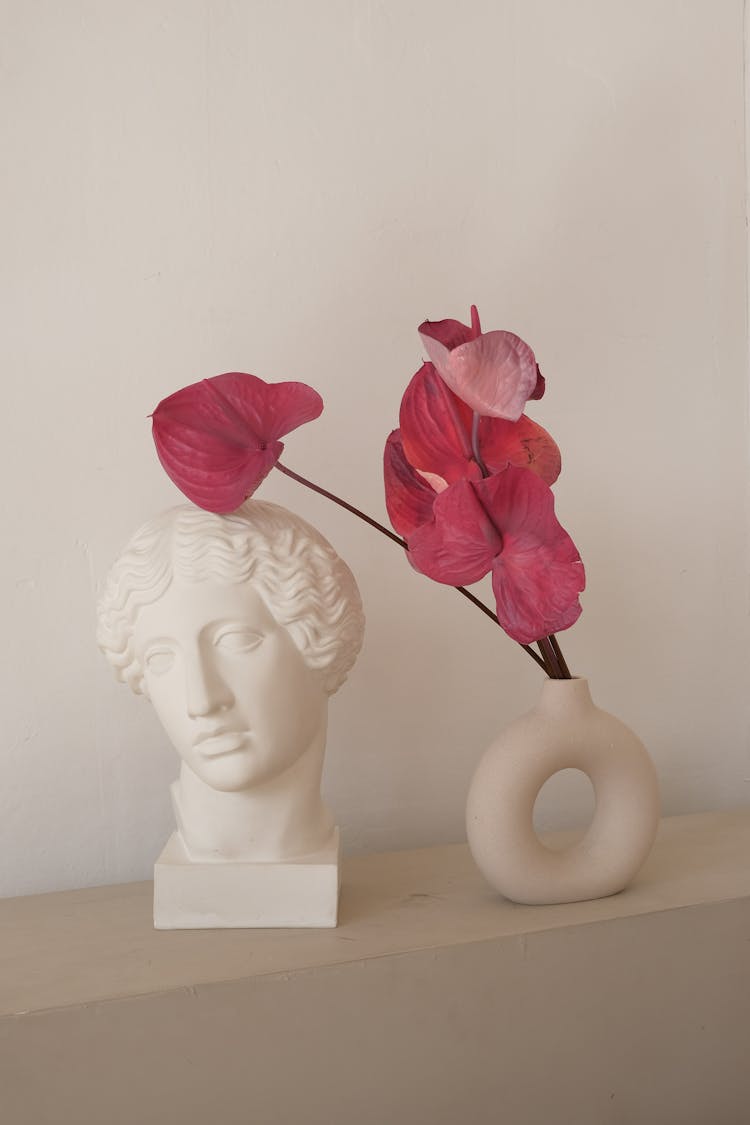 Sculpture Of Male Head Next To Vase Of Pink Anthurium Flowers