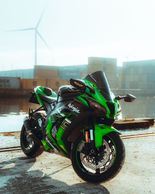 Free A vibrant green sports motorcycle parked near an industrial area with wind turbines in the background. Stock Photo