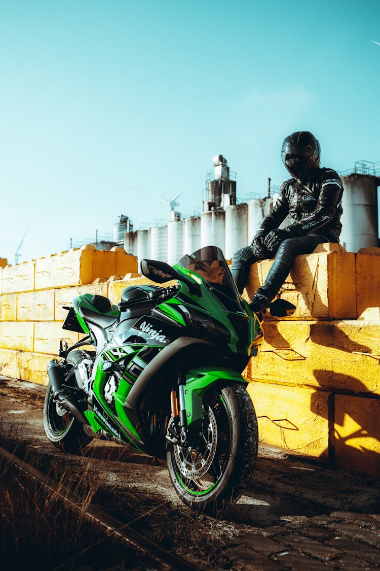 Man In Black Motorcycle Suit Sitting Near His Green And Black Sports Bike