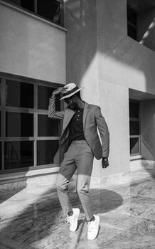Fashionable man in a suit and hat, captured in black and white, strikes a pose indoors.